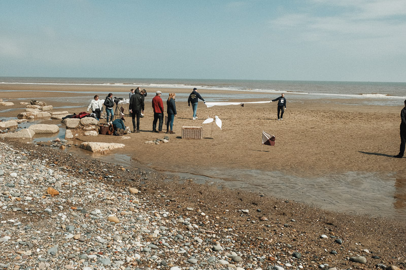 The project team and performers preparing for the performance on the beach. There is equipment around.