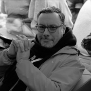 Black and white photograph of Christian Billing smiling at the camera with his hands clasped together